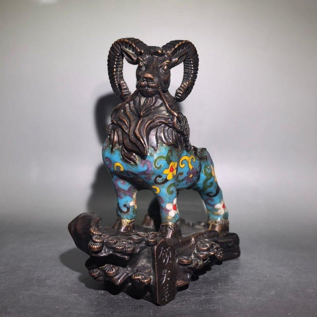 A striking Chinese Cloisonné enamel sculpture of a ram. The figure is depicted standing on a stylized bronze-colored...