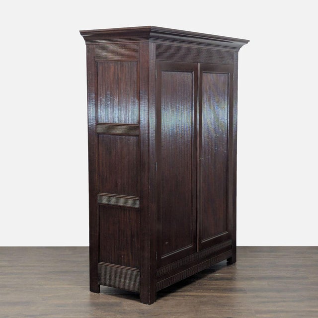 This Kerry Joyce hutch and armoire features a classic dark wood finish and elegant double doors with a textured design....