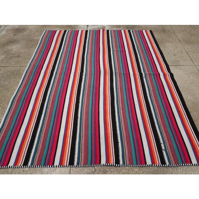 This Mid-20th century Turkish Flatweave Kilim rug, presents a vibrant and rhythmic composition of vertical stripes in...