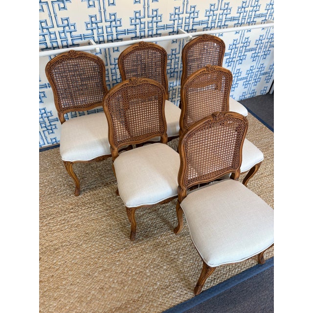 Set of 6 French Louis XV style dining chairs with carved wood frames and cane backs. Newly upholstered seats in a neutral...