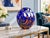 A striking art glass vase featuring a rich cobalt blue body decorated with flowing white, terracotta, and dark olive...