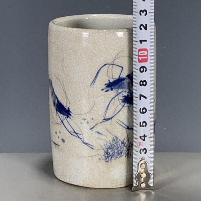 A charming Chinese blue and white porcelain brush pot (bitong). The cylindrical vessel features a creamy, all-over crackle...