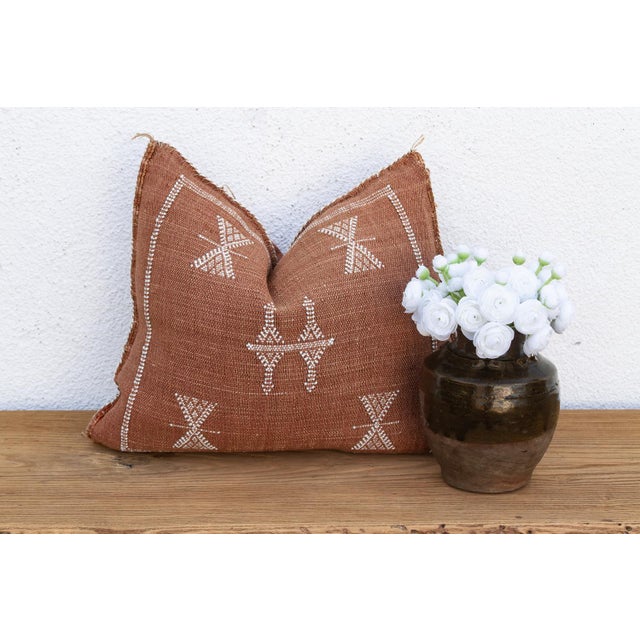 A pair of stick-figure medallions link hands at the center of this handcrafted Moroccan cactus silk pillow, framed by four...