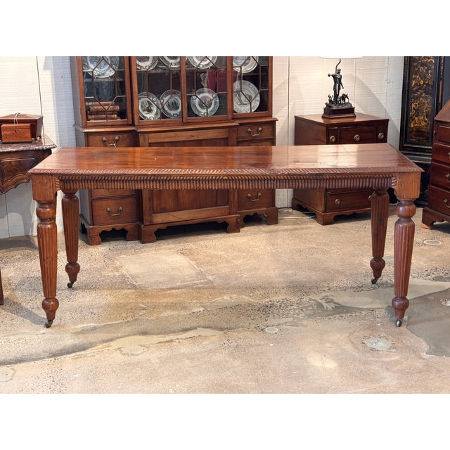 A long mahogany table with a richly carved apron — a continuous gadrooned border runs the full length, with carved corner...