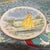 This vintage porcelain collector plate features a beautifully detailed illustration of a woman dressed in a vibrant yellow...