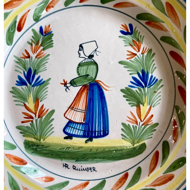 A fabulous antique HR Quimper charger or large plate featuring a petit Breton woman in the center and an a la touche...