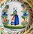 A fabulous antique HR Quimper charger or large plate featuring a petit Breton woman in the center and an a la touche...