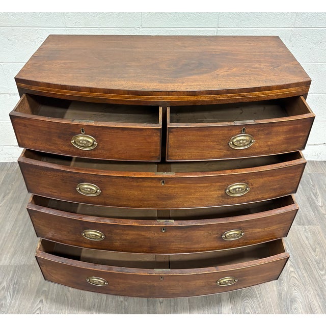This is an elegant antique Federal Hepplewhite style bowfront mahogany chest or dresser from the 19th century, likely...