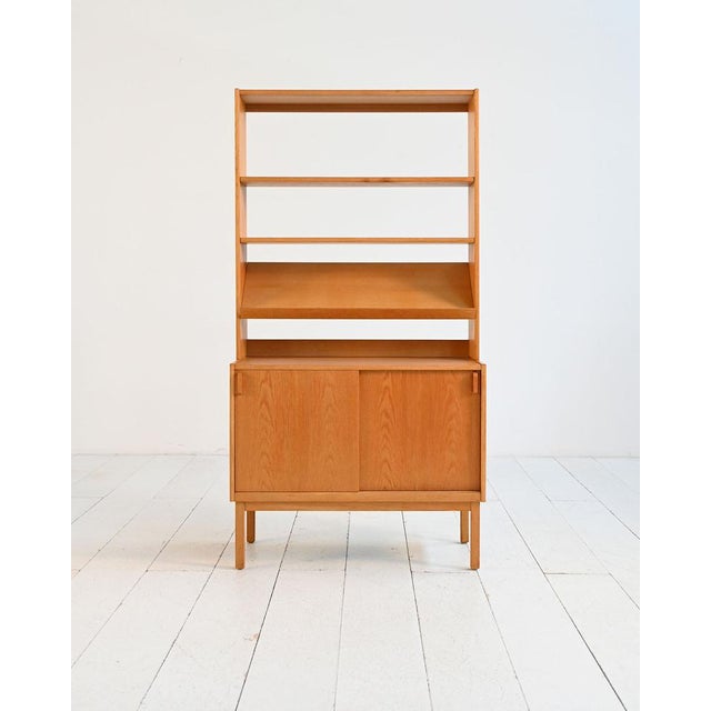 Oak bookcase featuring a storage unit with sliding doors and an open upper structure with adjustable shelves. Designed by...