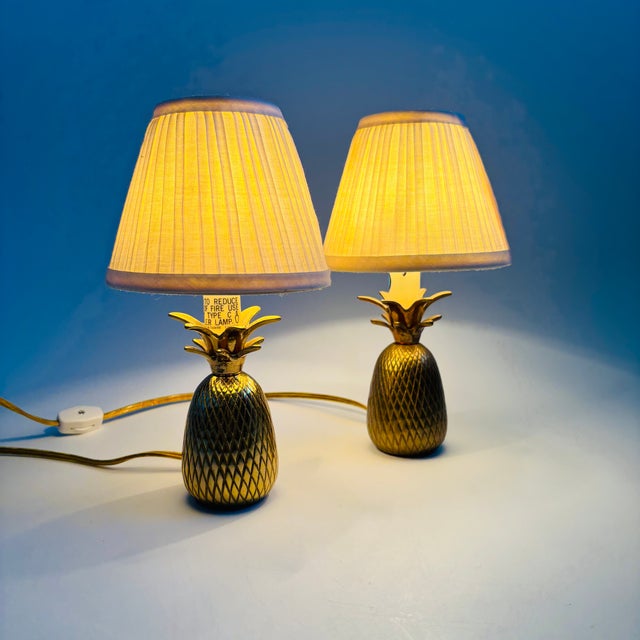 A pair of small vintage table lamps with brass bases in the shape of pineapples. Pleated white shades are included. Each...