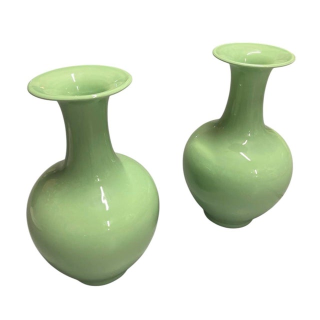 This elegant pair of mid-century modern style porcelain vases showcases a striking monochromatic celadon green glaze with...