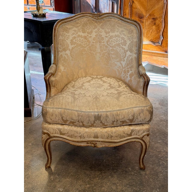 A Louis XV style bergere with a shaped upholstered back, outscrolled arms, and a loose seat cushion, raised on cabriole...