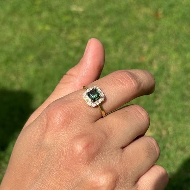 This Halo ring showcases a striking 1.22 carat green tourmaline set in 14K yellow gold. The tourmaline measuring 5.5 x 5.5...