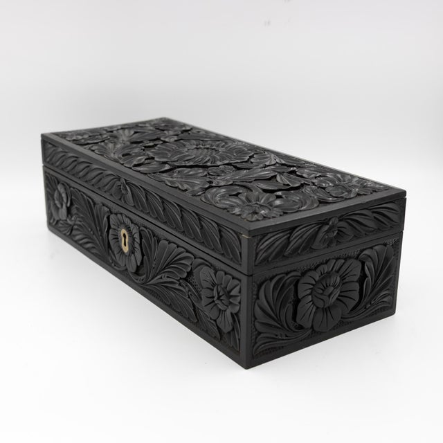 An Anglo-Indian glove box, circa 1850. The rectangular case is solid ebony, carved in low relief with a central sunflower...