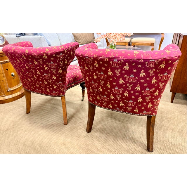A striking pair of tufted chinoiserie style accent chairs upholstered in a vivid red fabric with gold figural and scenic...