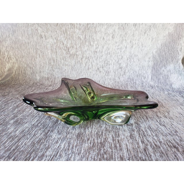A beautiful hand-blown bowl in green with a deep orchid purple. The top boasts graceful lines reminiscent of a flower in...