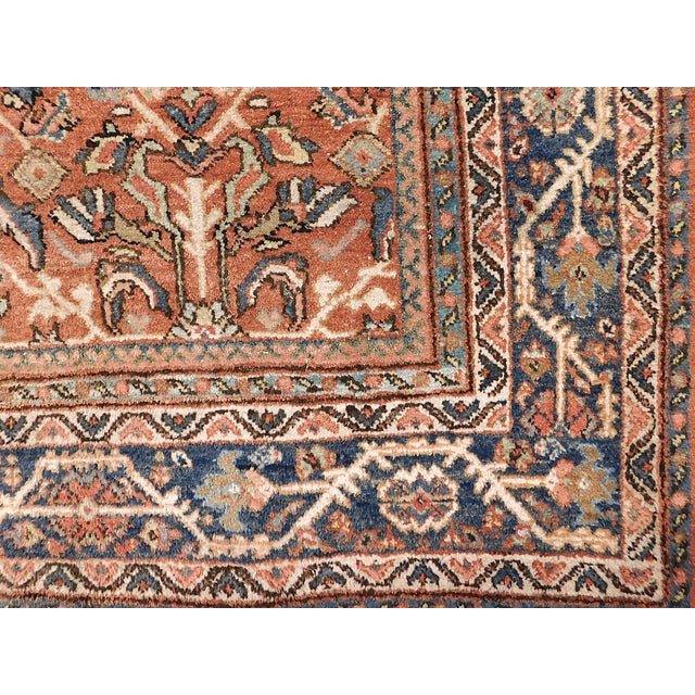 Rust field decorated with geometric motifs and stylized flowers, within a blue border. Wool pile on cotton foundation....
