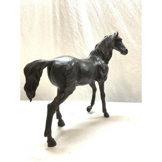 A tall dark bronze horse sculpture with a rich dark brown patina, depicted in a walking pose with forelegs extended in a...