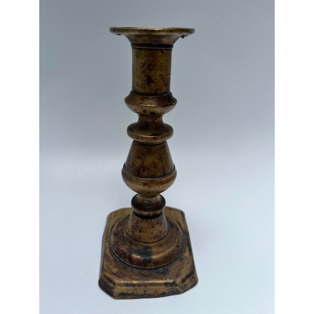 A single antique brass candlestick with rectangular base and pierced cup.
