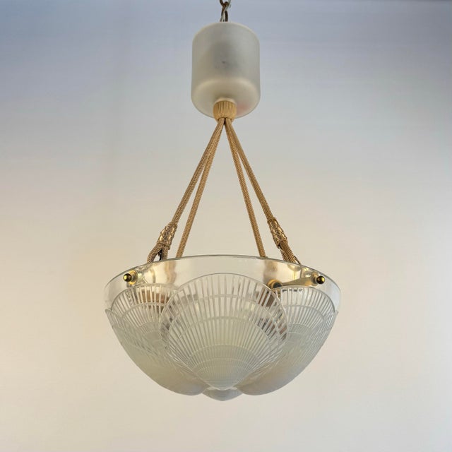 A beautifully sculpted glass shade with layered coquille detailing suspended from elegant braided cords with refined brass...