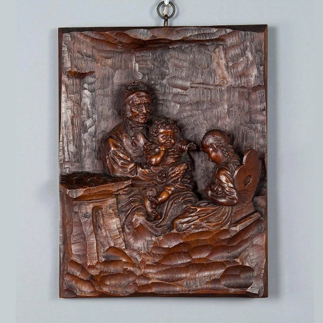 The wooden carved relief shows a grandfather with grandson on his lap. The granddaughter is sitting on the chair and hides...