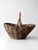 A vintage wicker gathering basket with a softly tapered silhouette and twisted overhead handle, woven in warm natural...