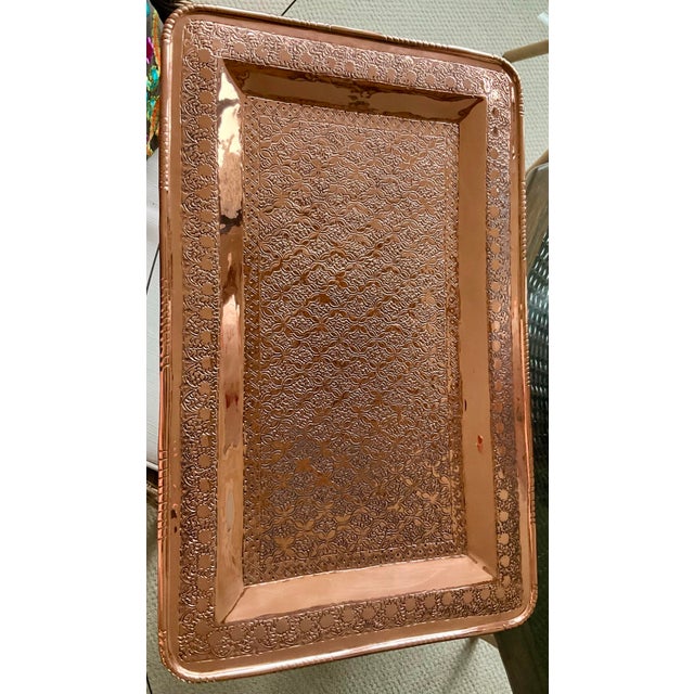 The copper tray has a shiny, professionally polished finish. It features intricate, hand embossed Moroccan-style patterns...