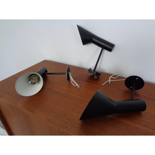 Three black AJ Visor wall lamps, designed by Arne Jacobsen for Louis Poulsen in 1958. Two lamps are without switches, and...