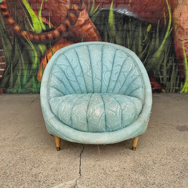 Mid-century clam shell chair with tufted blue fabric and wooden legs.