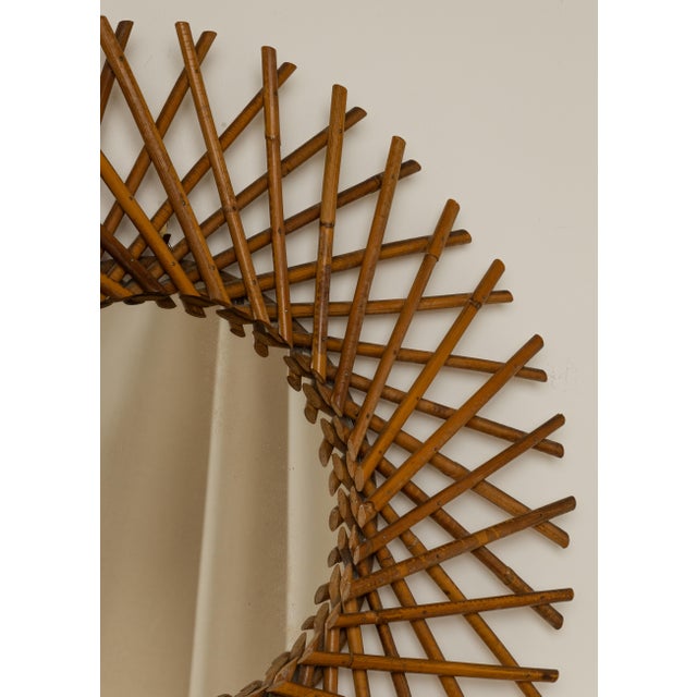 Round rattan wall mirror with radiating crossed-stick sunburst frame. Italian Mid-Century Modern, circa 1960s. Original...