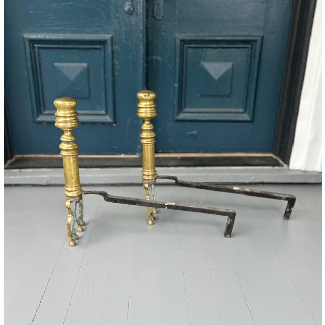 A handsome and well-proportioned pair of antique brass fireplace andirons featuring classic turned columnar shafts and...