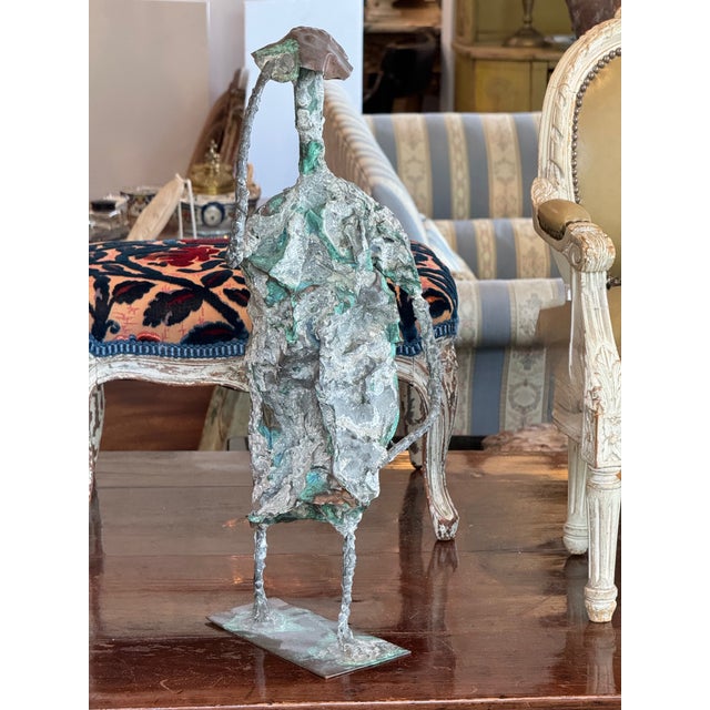 Expressive abstract sculpture formed from welded metal with heavy texture and a greenish patina. The figure is loosely...