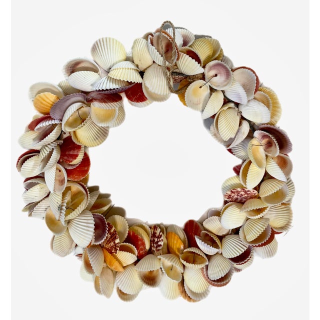 A handmade seashell wreath comprised of individually strung scallop shells in ivory, rust, yellow and dark red tones.