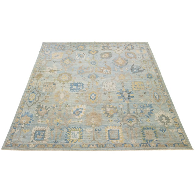 This hand-knotted wool rug has a light blue background adorned with brown and yellow accents in an all-over design. This...