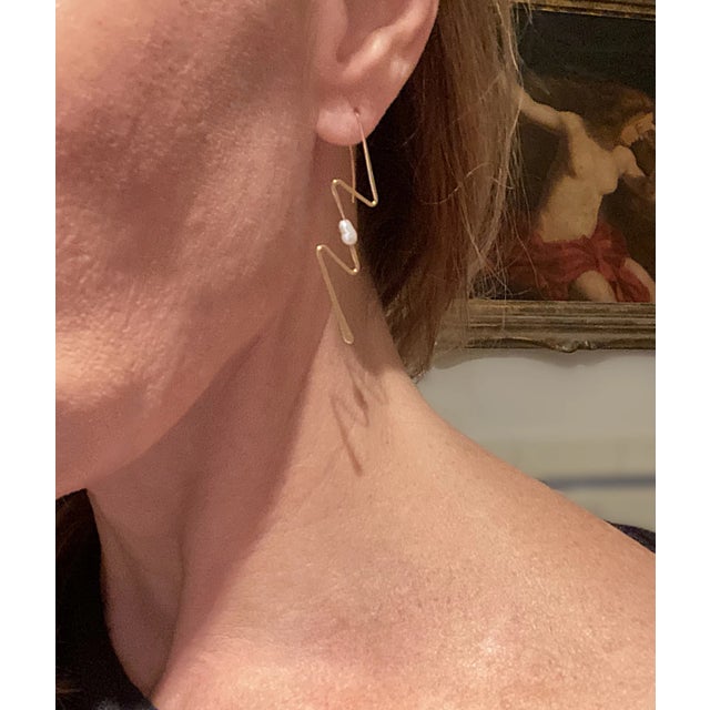 A pair of 14-karat yellow gold lightning bolt earrings with freshwater pearl accent at center. Excellent condition as...