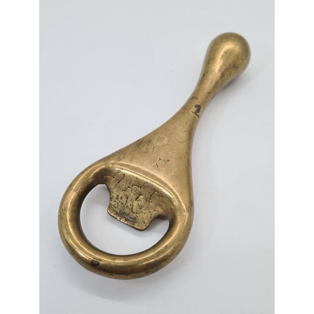 An elegant, vintage bottle opener made of solid brass, featuring the modernist aesthetic characteristic of mid-century...