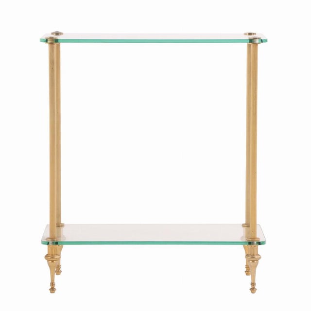 A refined pair of mid-century French end tables, each featuring a sleek brass cylindrical legs supporting two tiers of...