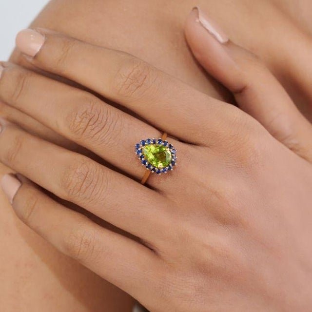 This elegant cocktail ring features 2.39ct of peridot & blue sapphire, set in 18k yellow gold. The pear-shaped center...
