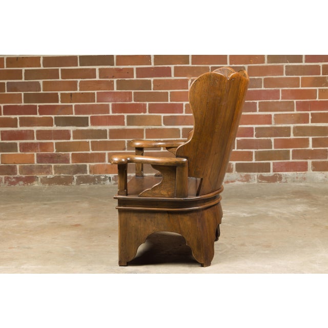 A rustic English walnut lambing chair from the 19th century with curving arms and carved base. Whisk your home's ambiance...