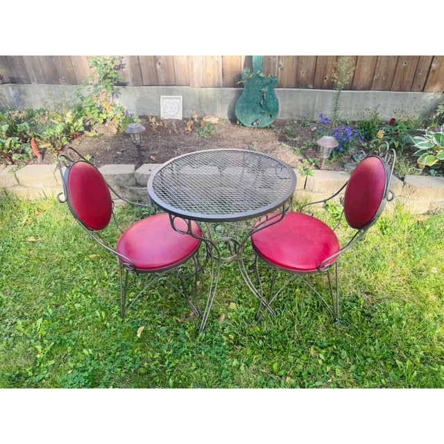 A striking 1960s bistro set by Syd Leach, consisting of two wrought iron chairs and a coordinating round mesh-top table....