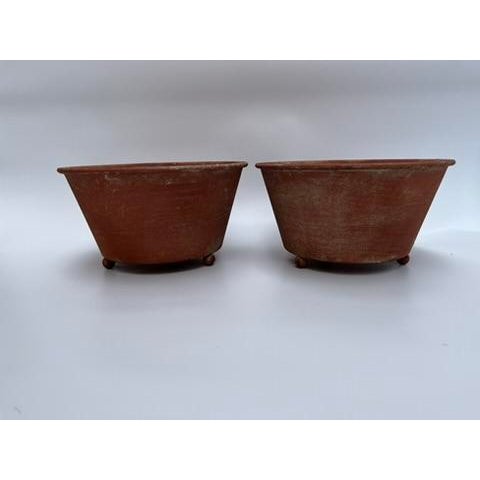 A matching pair of round tole bowls or cachepot featuring a terra cotta style finish and three ball feet.