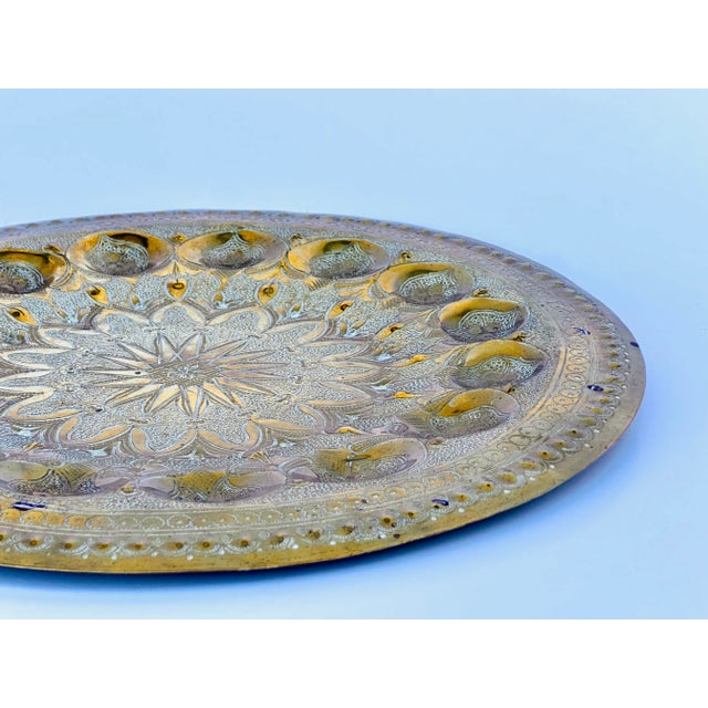 Vintage brass tray with intricately tooled surface and round form. Integrated brass hook affixed on the back for hanging.