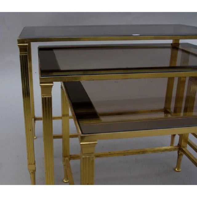 Set of three nesting tables in gilt metal, with fluted legs supporting a smoked glass top. Work from the 20th century.