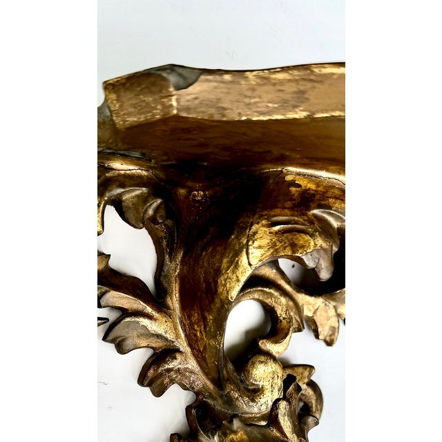 A striking pair of Rococo-style giltwood wall brackets featuring acanthus leaves and flowing scrollwork beneath shaped...