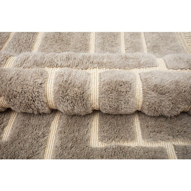 A labyrinth traced in wool, endlessly winding. Crisp ivory pathways interlock across a deep taupe field, forming an...