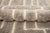 A labyrinth traced in wool, endlessly winding. Crisp ivory pathways interlock across a deep taupe field, forming an...
