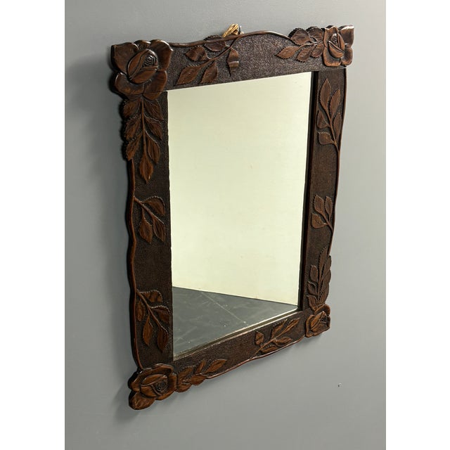 Wall mirror in a dark stained wooden frame, carved by hand with a rose in each corner and sprays of serrated leaves along...