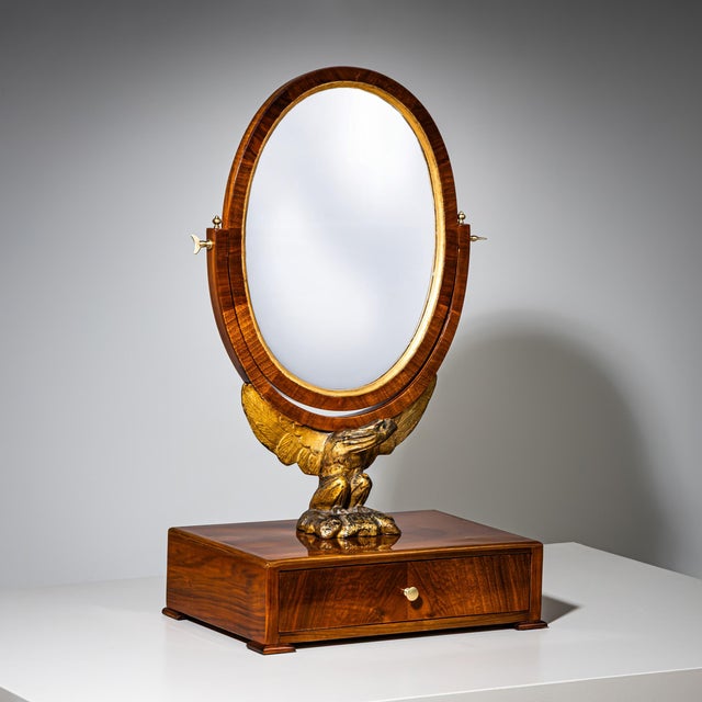 Biedermeier table mirror with a drawer and a tilting oval mirror plate supported by a carved, partially gilt eagle. The...