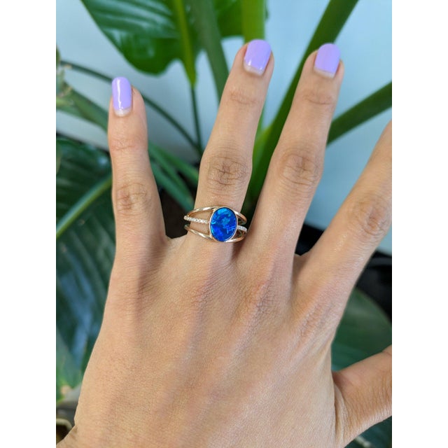 A solid natural boulder opal cabochon flashes with vivid play of color in a freeform oval at the centre of this solid 14K...