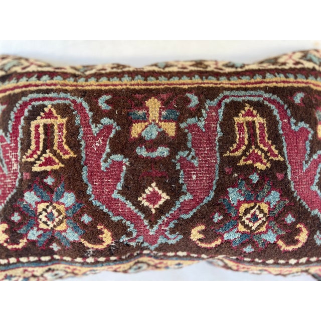 This is a pillow upholstered in a 19th century rug fragment, featuring charming tribal motifs. There is wear on some areas.
